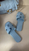 Pair of light blue sandals next to a matching quilted handbag on a beige surface.